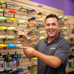 Staff member Tyler James in front of the lure wall pointing out topwater baits and terminal tackle